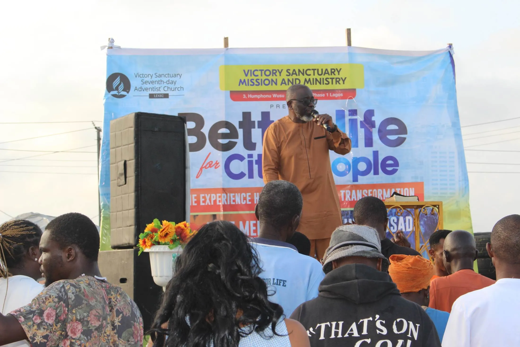 A Victory Sanctuary pastor speaking to a crowd under a Better Life for City People banner