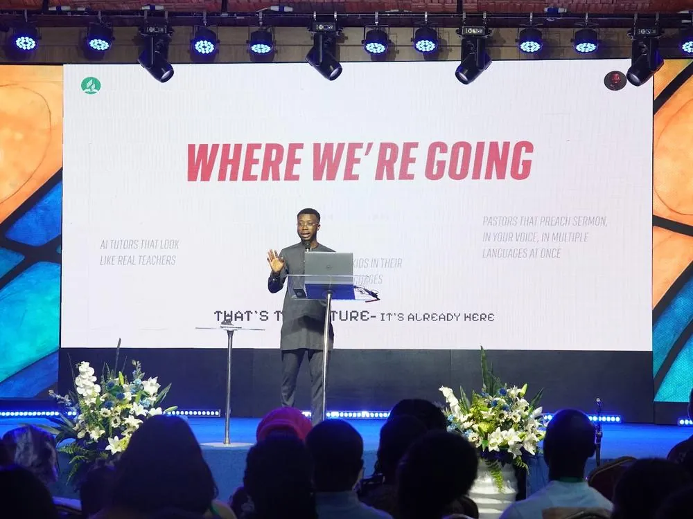 A speaker on stage in front of a screen that reads Where we're going