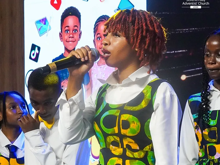 Two girls in matching print dresses singing on stage at Children’s Day 2026
