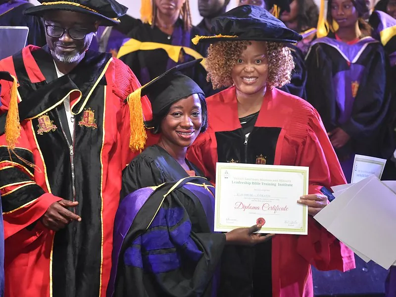 A graduate smiling with her diploma at the Bible school graduation
