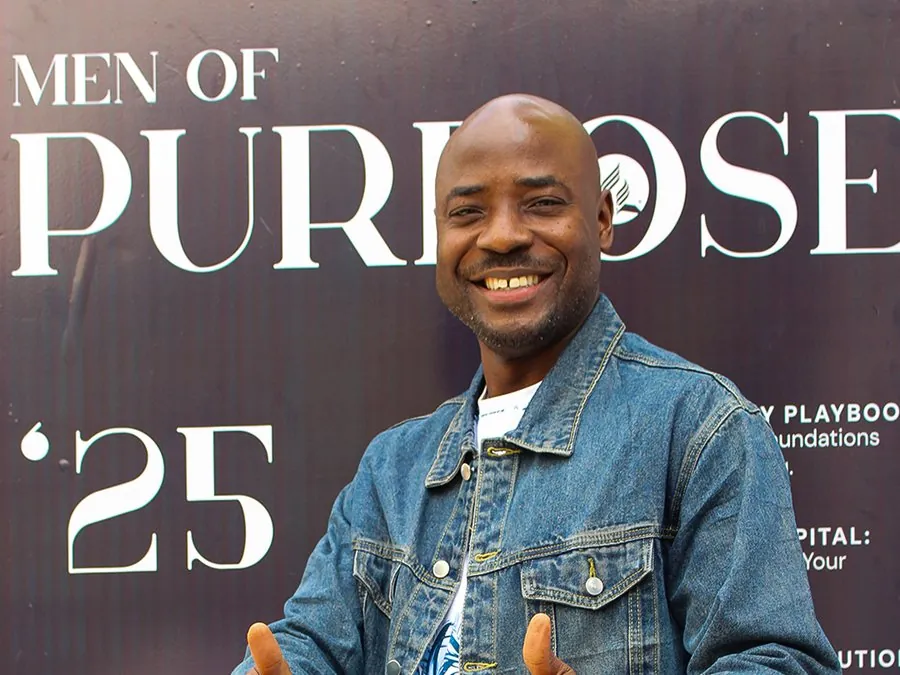 A smiling man giving two thumbs up in front of the Men of Purpose backdrop