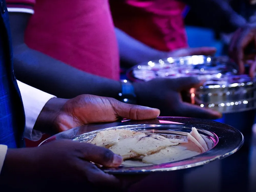 Hands holding a silver plate of communion bread