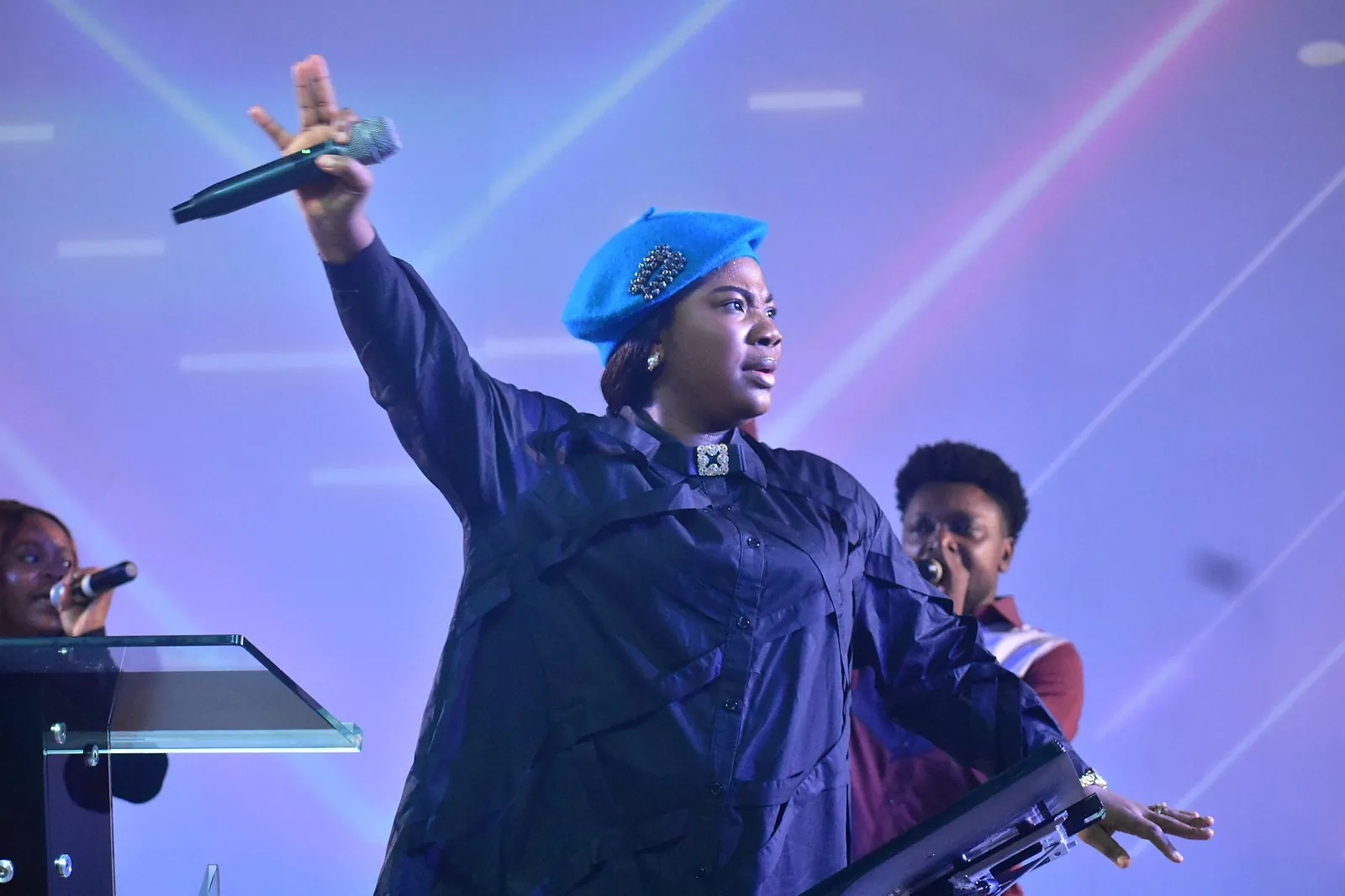 A minister in a blue beret with her arm raised high in praise