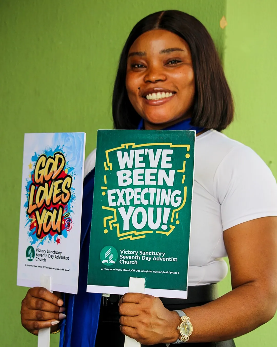 A smiling member of the welcome team holding signs that say We’ve been expecting you and God loves you