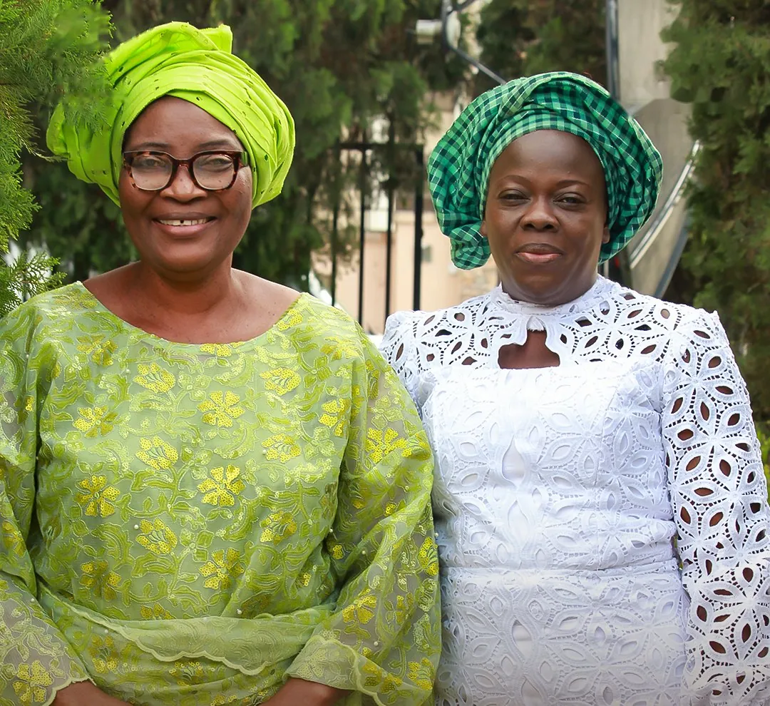 Two women of King’s Daughters smiling together, one in lime green and one in white lace