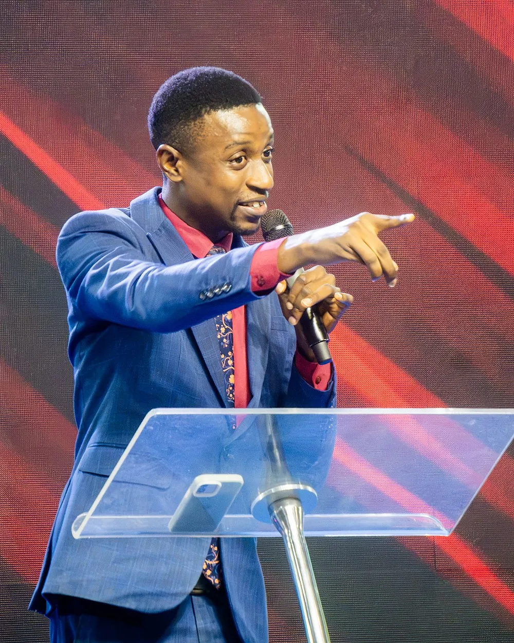 Pastor Victor Oyawoye in a blue suit, preaching from the pulpit