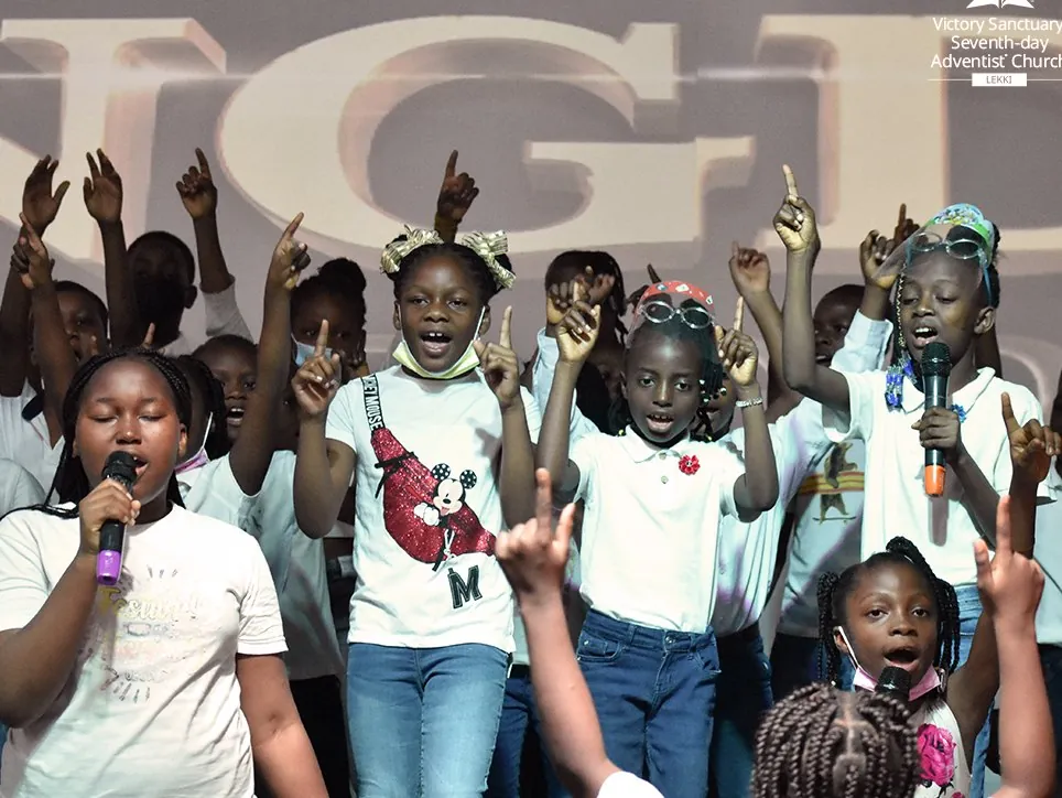 Children with their hands raised, singing on stage