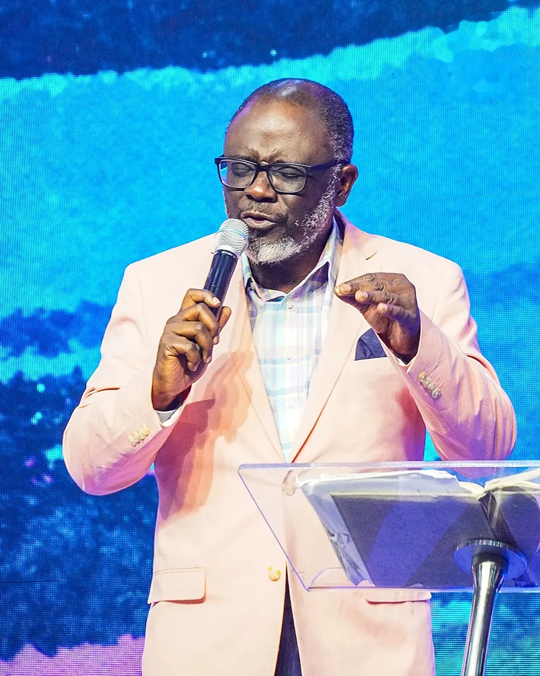 Pastor Bukky Ajide in a pink blazer preaching from the pulpit