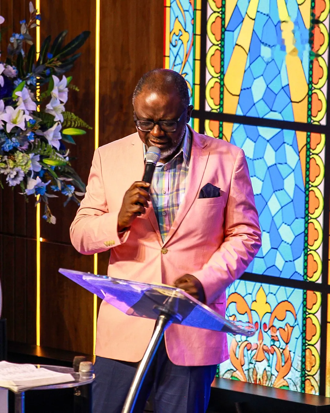 Pastor Bukky Ajide preaching from the pulpit beside the stained-glass window